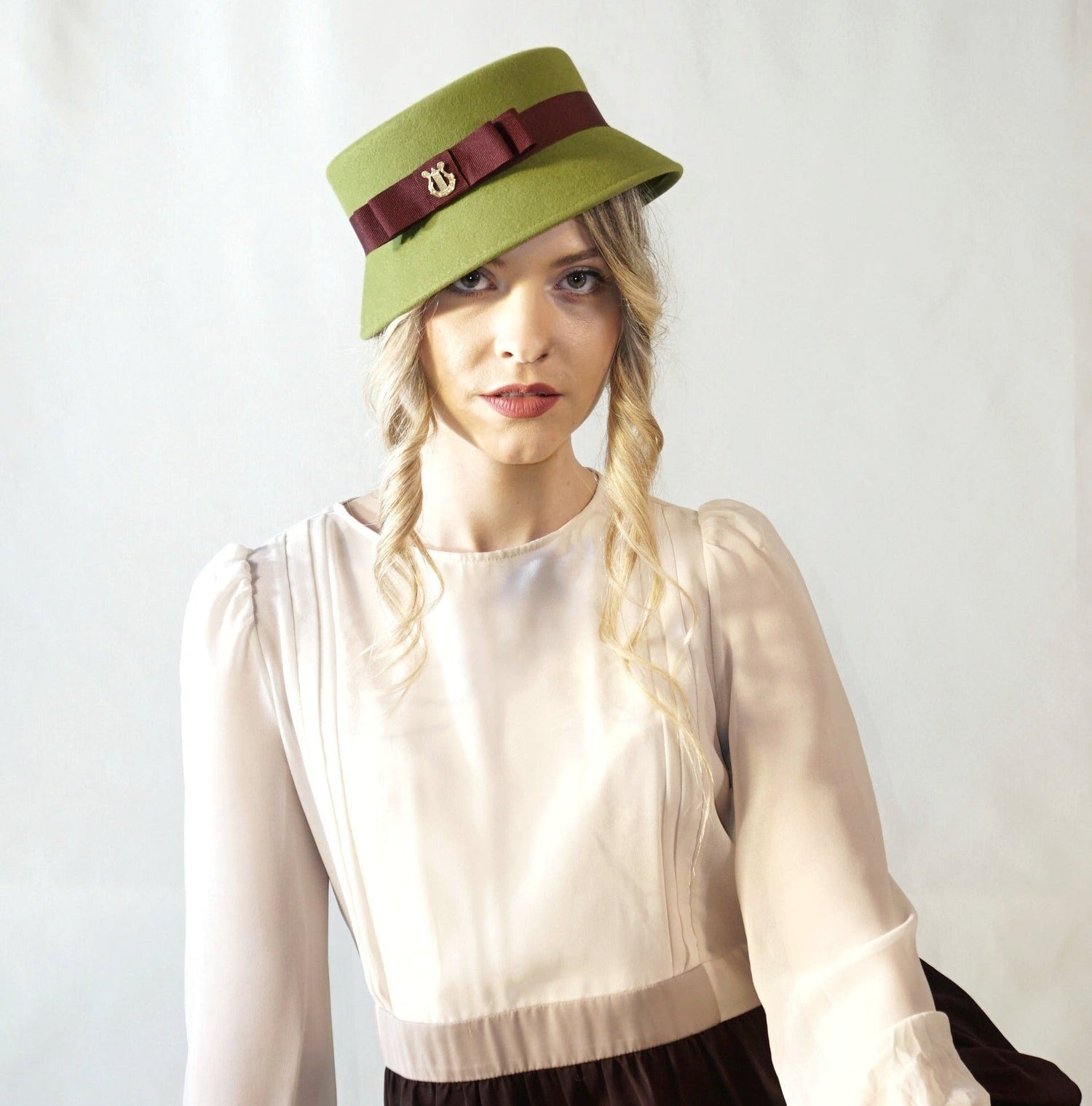 Evening Glamour Hats by Anna Xaniotaki. Couture pillboxes, fascinators,wide-brim & mini hats for weddings, race days. Meet Aristocratic Melody mini hat in pale green fur felt with burgundy front bow & lyre jewel.