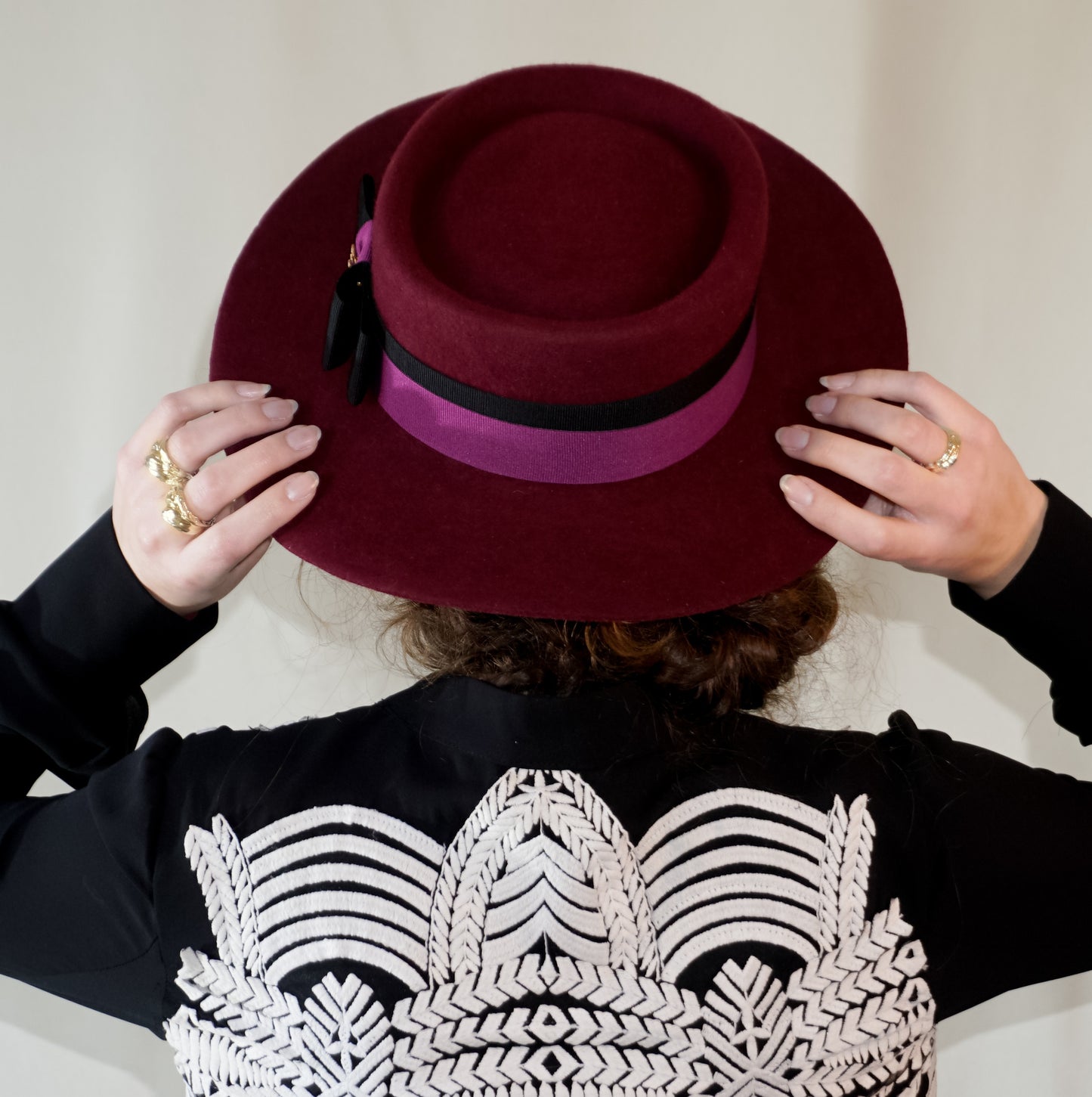 Woman wearing Scarlet Ode burgundy boater hat with black and orchid purple ribbons, double bow and golden lyre by Anna Xaniotaki - back close view