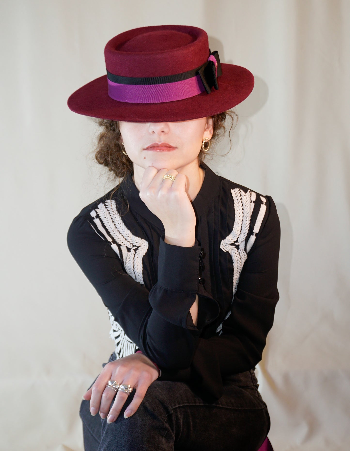 Woman wearing Scarlet Ode burgundy boater hat with double bow and golden lyre by Anna Xaniotaki - front view.