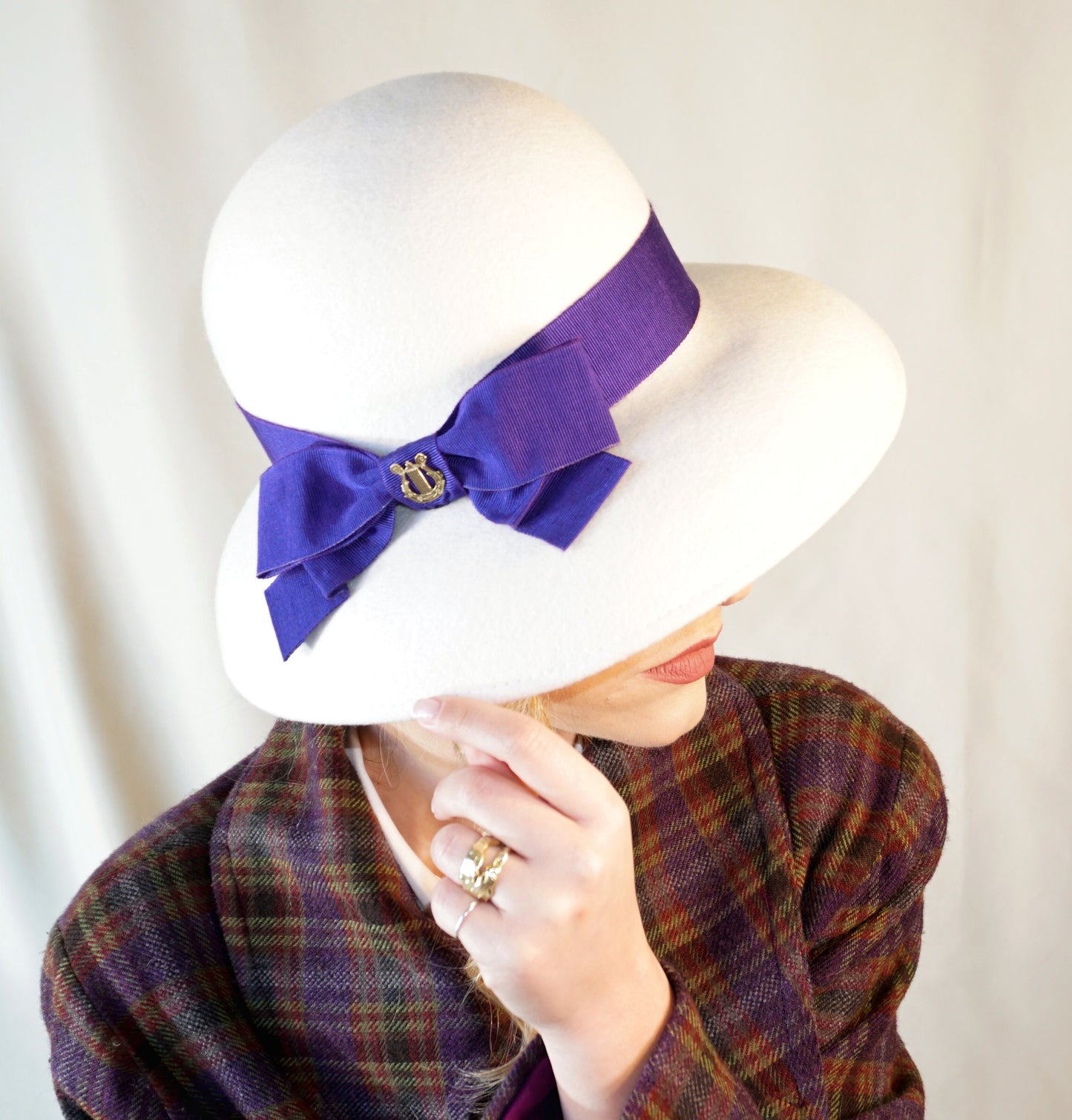 Blanche Élégance white felt hat with purple grosgrain bow and golden lyre by Anna Xaniotaki, right three-quarter front view