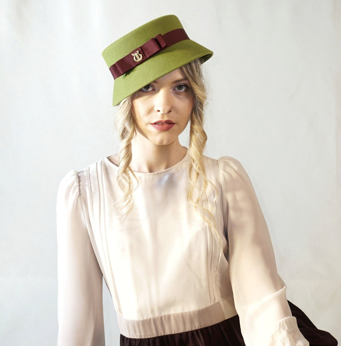 Aristocratic Melody lime pillbox felt hat with double burgundy bow and 14ct gold-plated silver lyre by Anna Xaniotaki - front view