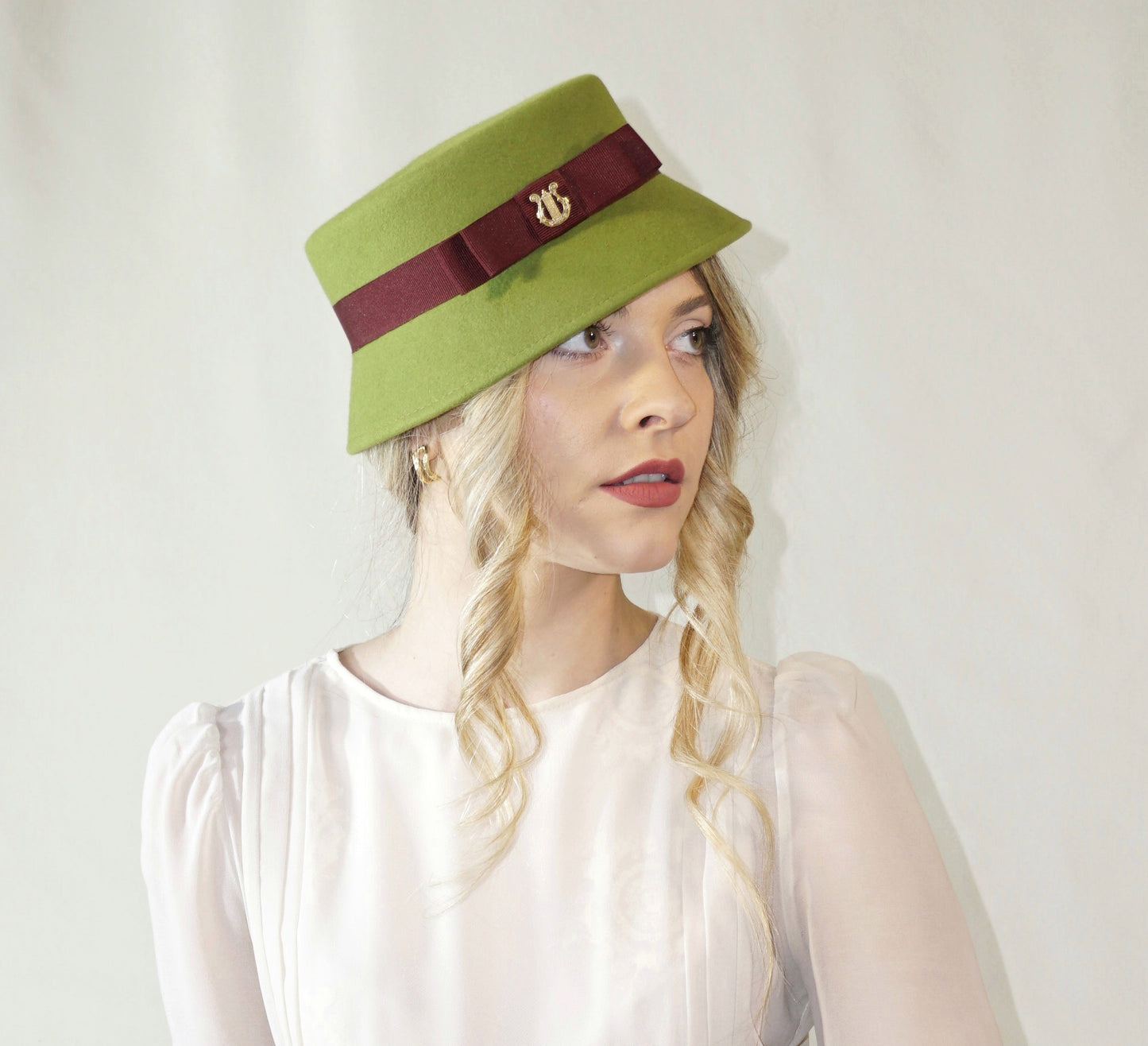 Aristocratic Melody lime pillbox felt hat with double burgundy bow and 14ct gold-plated silver lyre by Anna Xaniotaki - side angle view