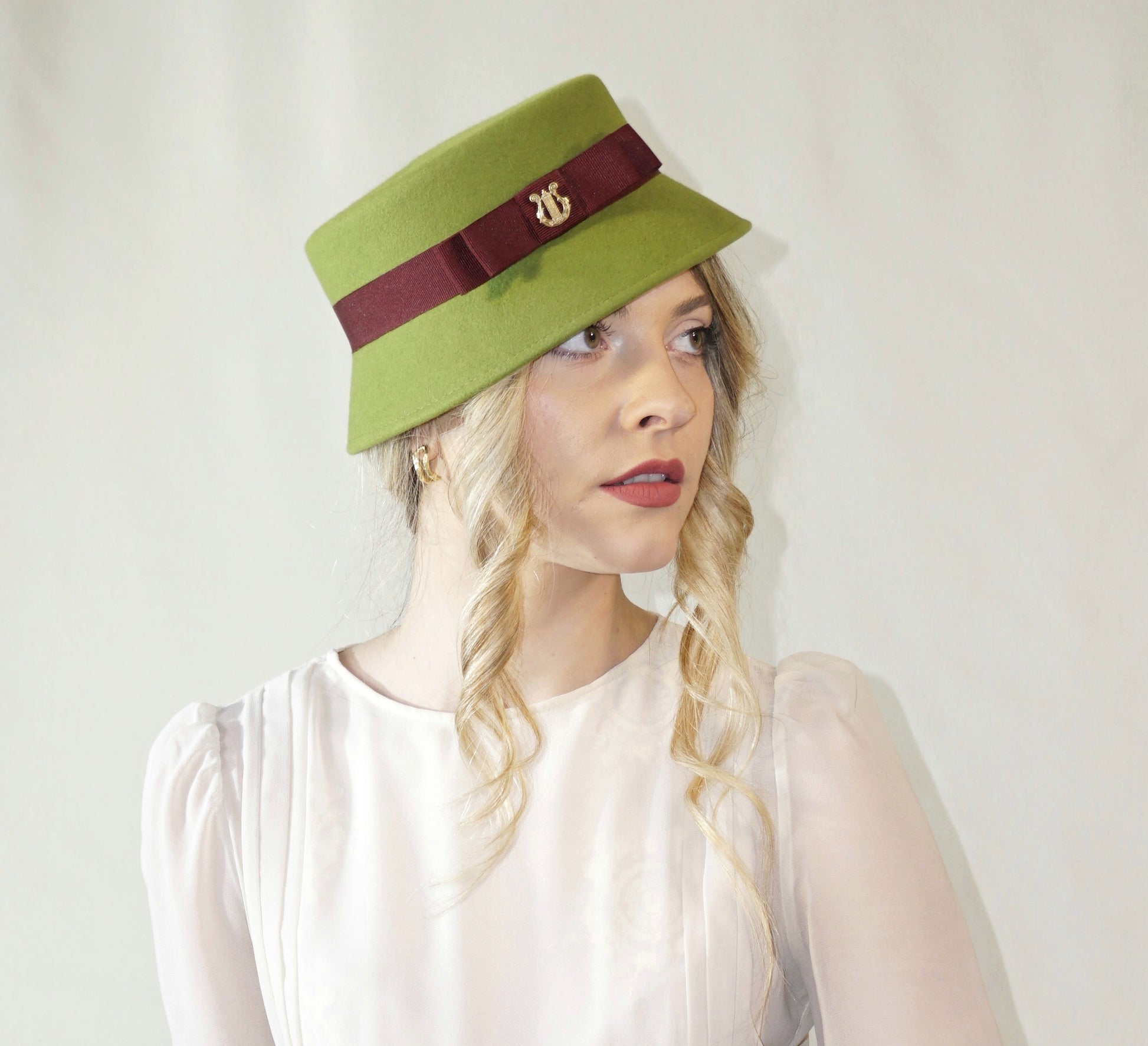 Aristocratic Melody lime pillbox felt hat with double burgundy bow and 14ct gold-plated silver lyre by Anna Xaniotaki - side angle view