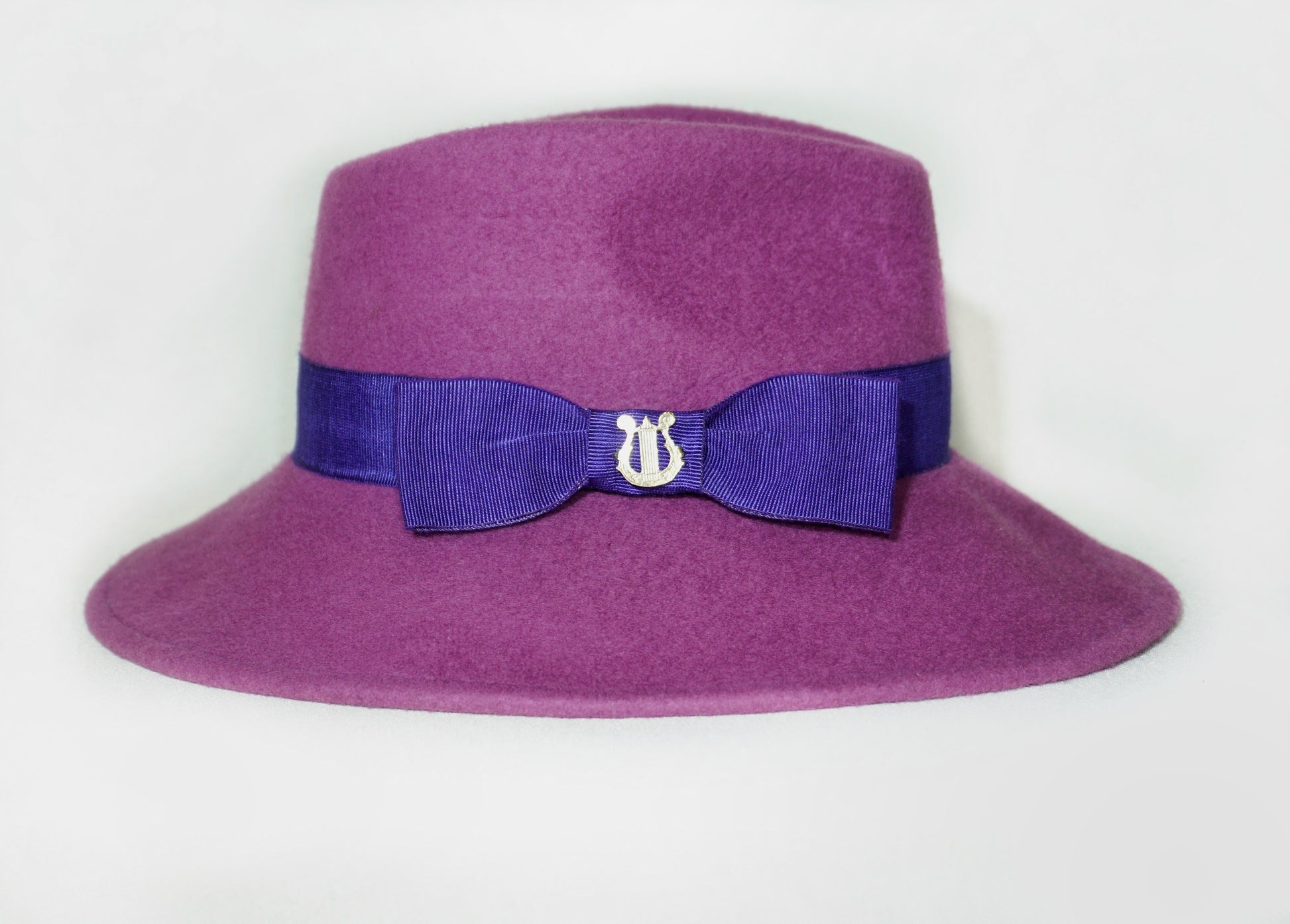 Right side view of the handcrafted Amaryllis fedora hat in luxury purple wool felt with a royal purple/ blue-violet Italian cotton grosgrain ribbon and the signature 14ct gold-plated sterling silver lyre jewel. Bespoke Couture Millinery by Anna Xaniotaki