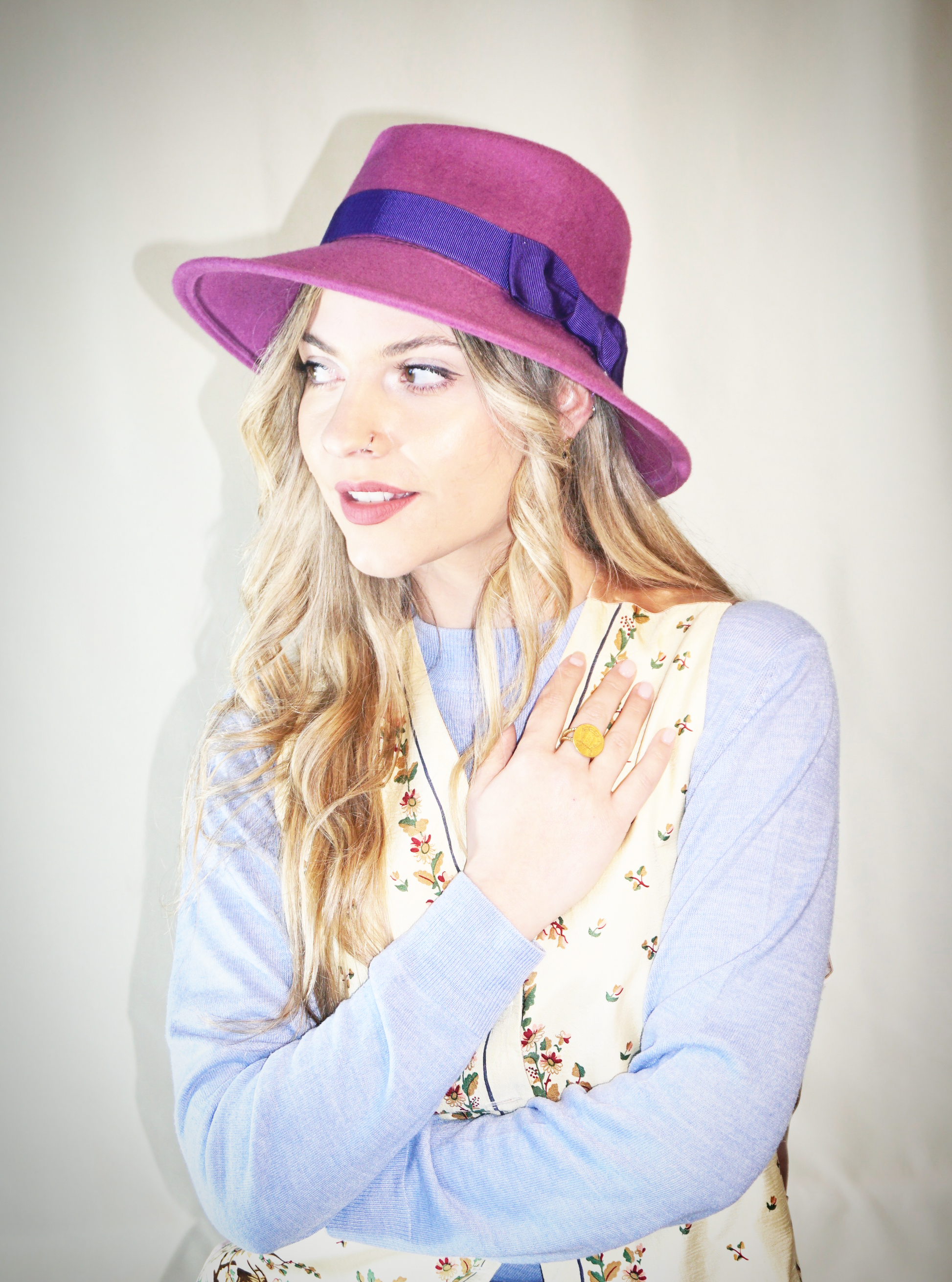 A woman poses in a three-quarter front left view, wearing the handcrafted Amaryllis fedora hat in luxury purple wool felt with a Royal Purple/Blue-Violet Italian cotton grosgrain ribbon band & bow. An ideal choice for everyday luxury elegance. Bespoke Couture Millinery by Anna Xaniotaki 