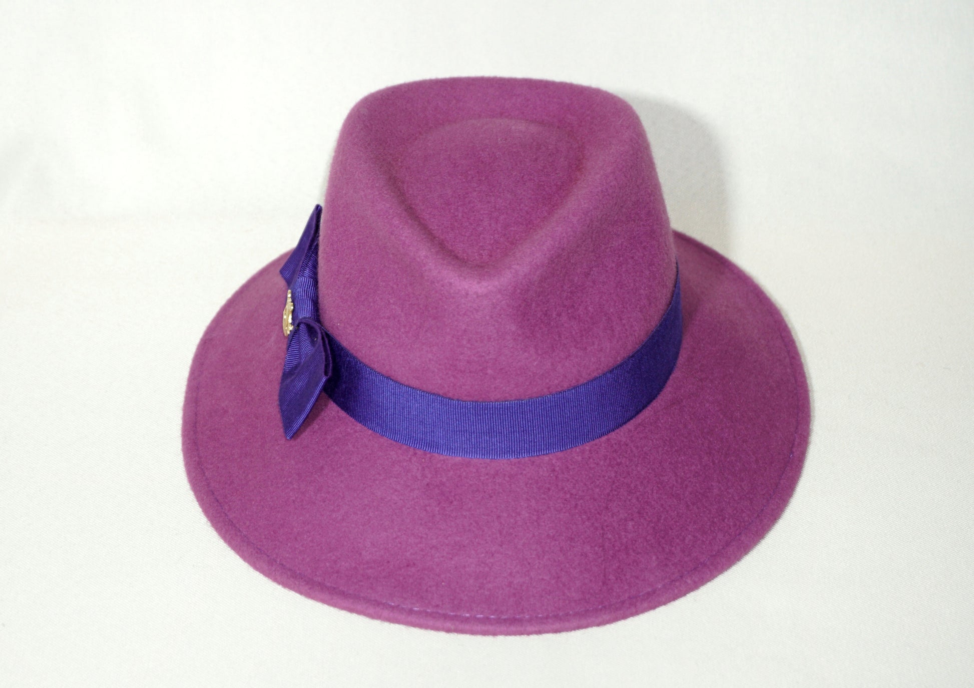 Front view of the handcrafted Amaryllis fedora hat in luxury purple wool felt with a royal purple/blue-violet Italian cotton grosgrain ribbon and the signature 14ct gold-plated sterling silver lyre jewel. Bespoke Couture Millinery by Anna Xaniotaki
