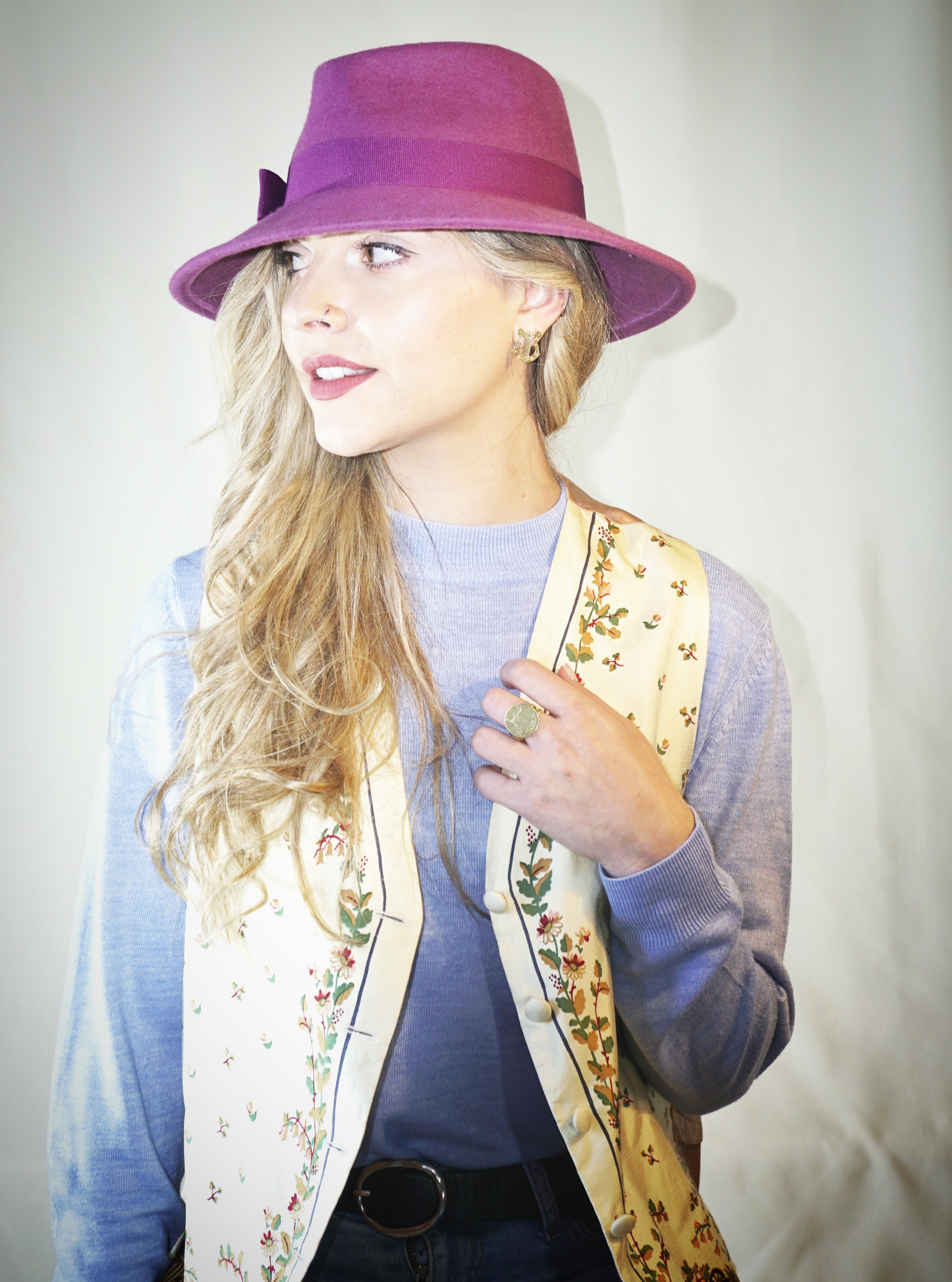 A woman poses in a three-quarter left side view, wearing the handcrafted Amaryllis fedora hat in luxury purple wool felt with a purple Italian cotton grosgrain ribbon bow. An ideal choice for everyday luxury elegance. Bespoke Couture Millinery by Anna Xaniotaki