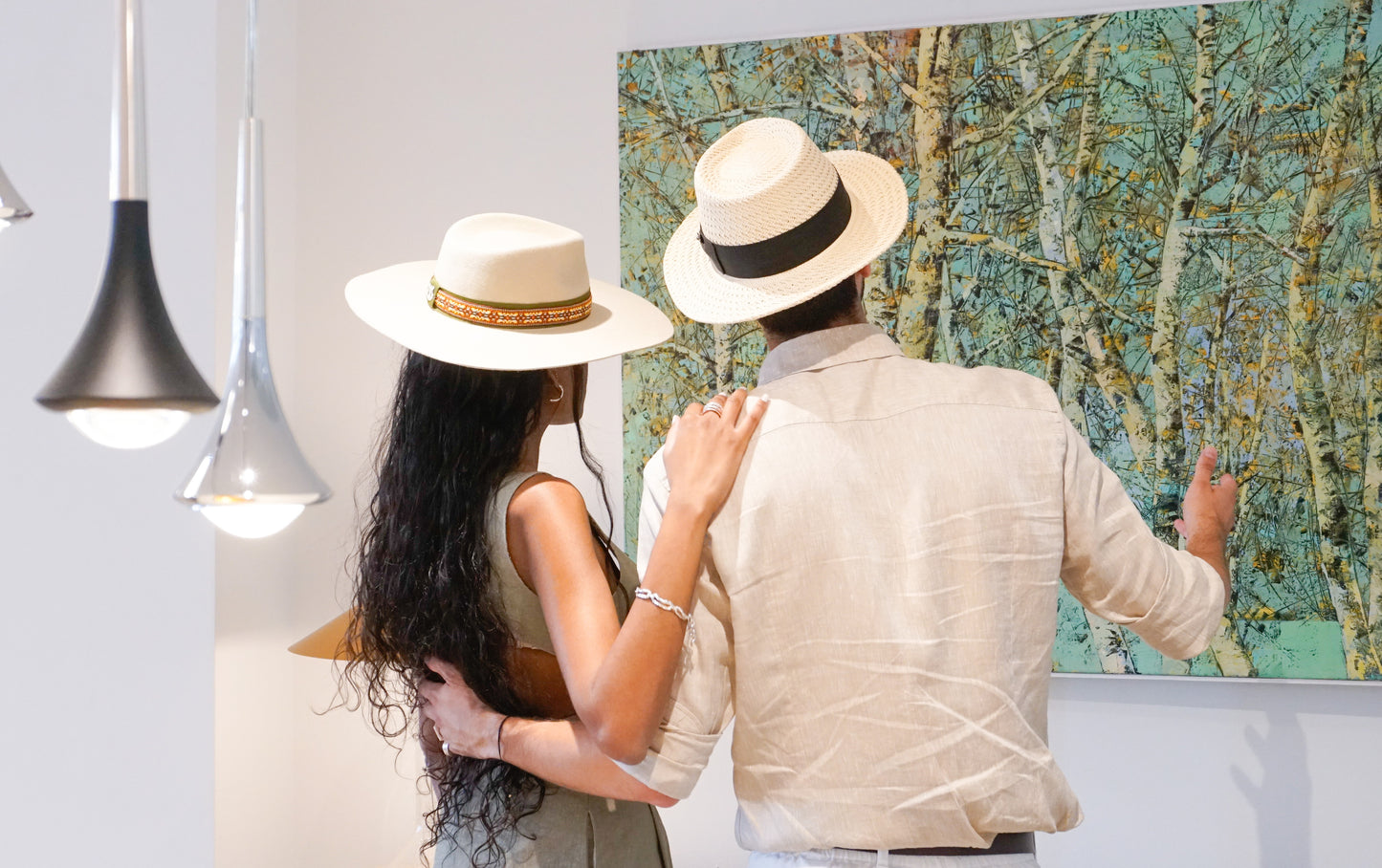Man wearing the André fedora straw hat in ivory with black Italian cotton grosgrain band, bow and 14ct gold-plated sterling silver lyre jewel, looking at a woman in a light cream fedora, back side view. Custom made-to-order fedora for summer special occasions, garden parties, vacations or for everyday man's elegance. Bespoke couture millinery by Anna Xaniotaki