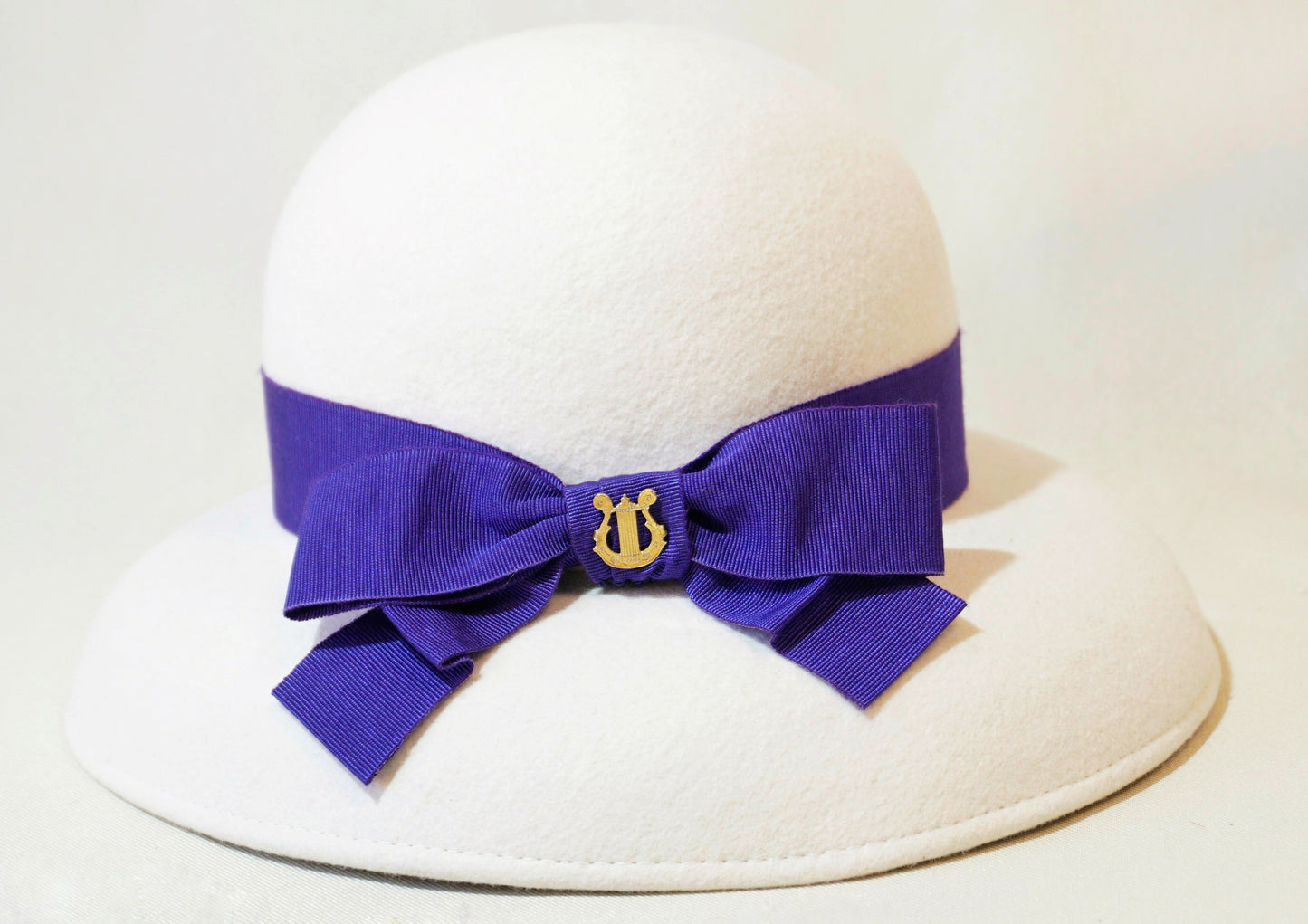 Blanche Élégance white felt hat with purple grosgrain bow and golden lyre by Anna Xaniotaki
