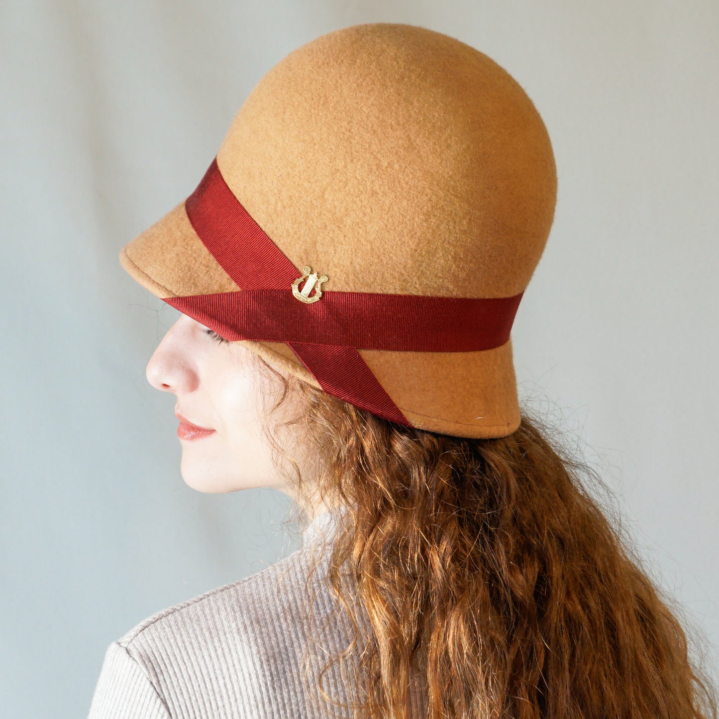 Daize cloche hat in camel wool felt with red ribbon and gold lyre detail by Anna Xaniotaki