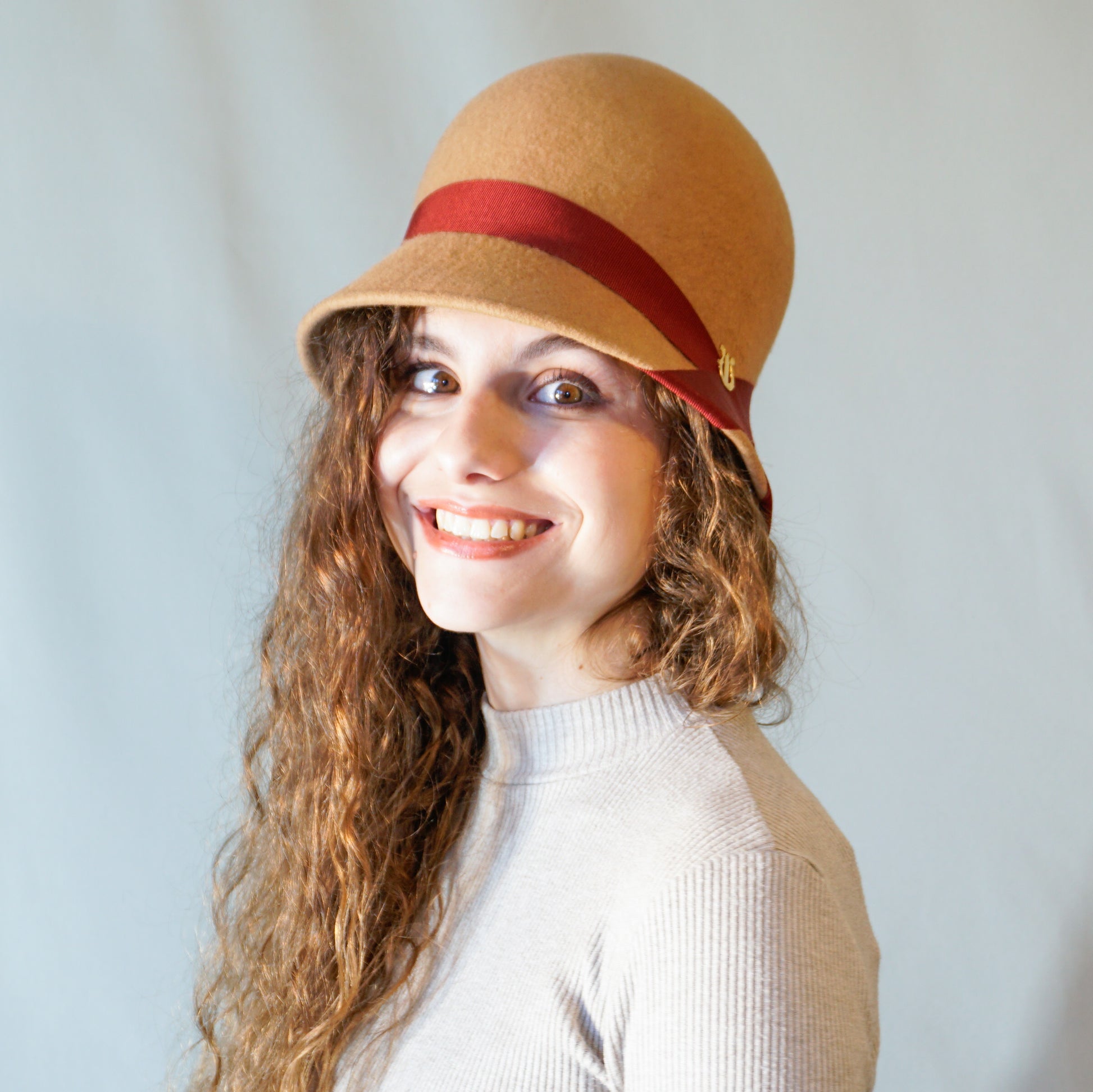 Daize cloche hat in camel wool felt with red ribbon and gold lyre by Anna Xaniotaki 