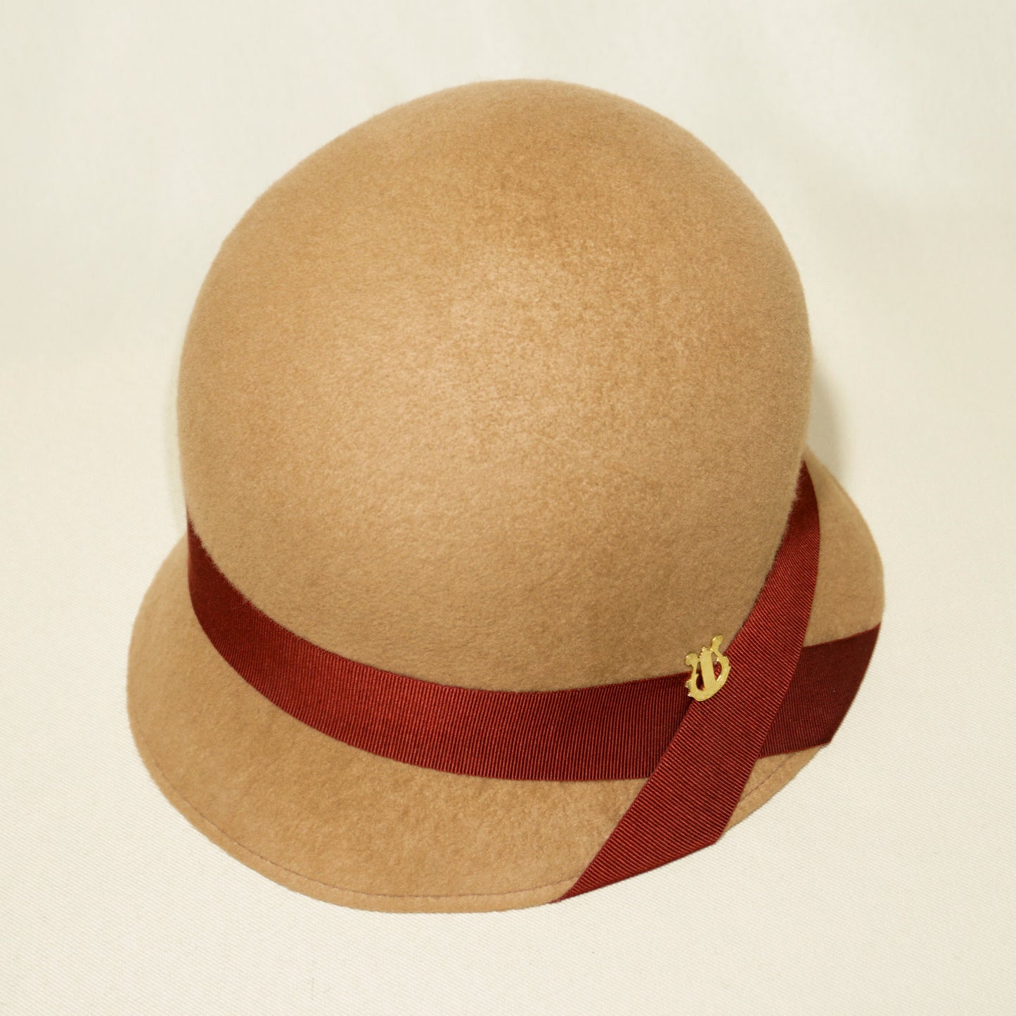 Daize cloche hat in camel wool felt with red ribbon and gold lyre by Anna Xaniotaki - three quarter view