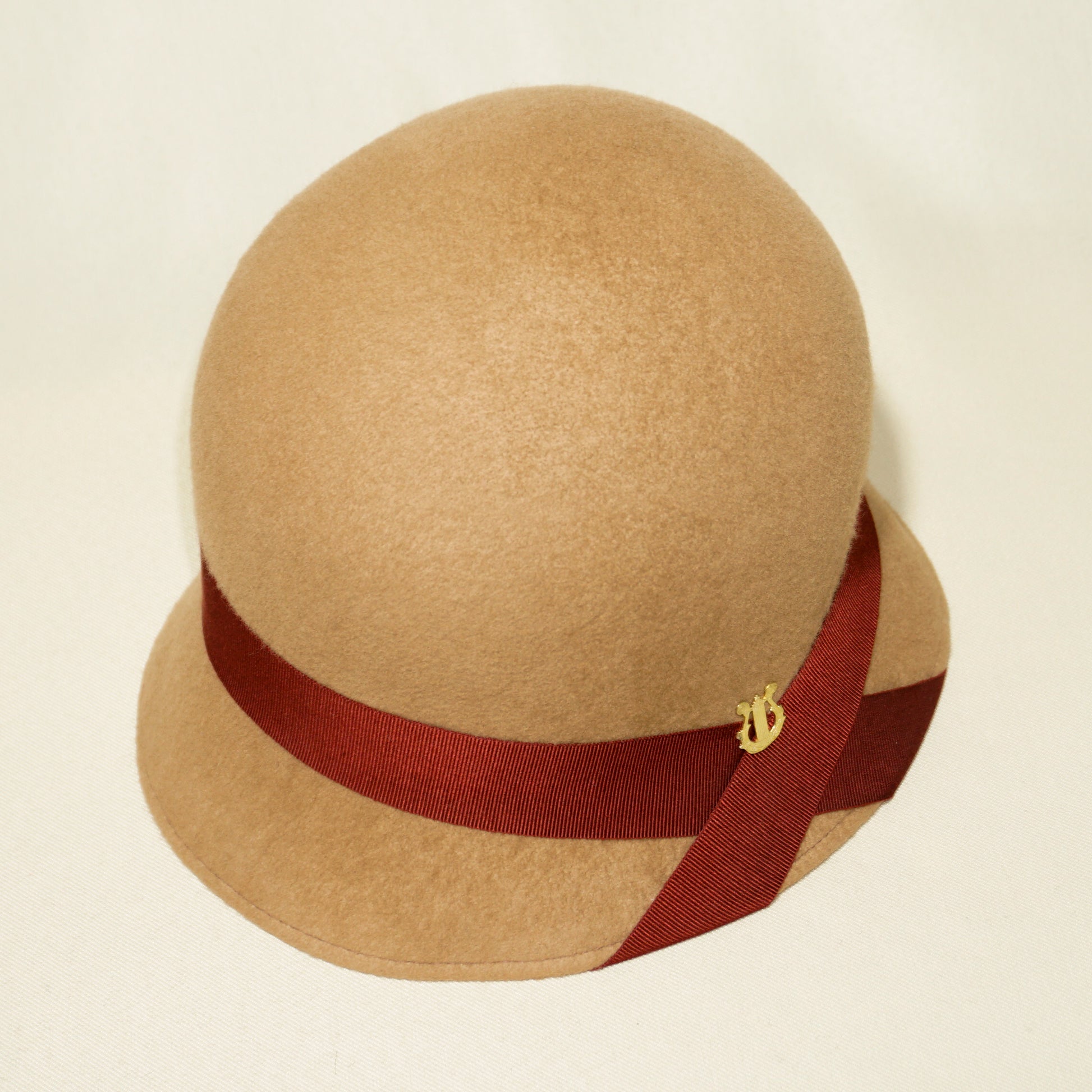 Daize cloche hat in camel wool felt with red ribbon and gold lyre by Anna Xaniotaki - three quarter view