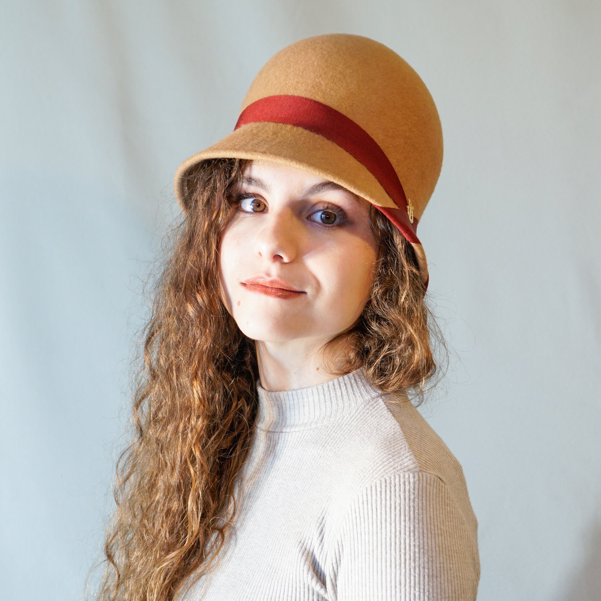 Daize cloche hat in camel wool felt with red ribbon and gold lyre by Anna Xaniotaki 