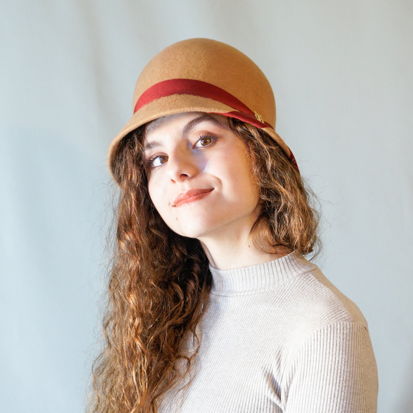 Daize cloche hat in camel wool felt with red ribbon and gold lyre by Anna Xaniotaki