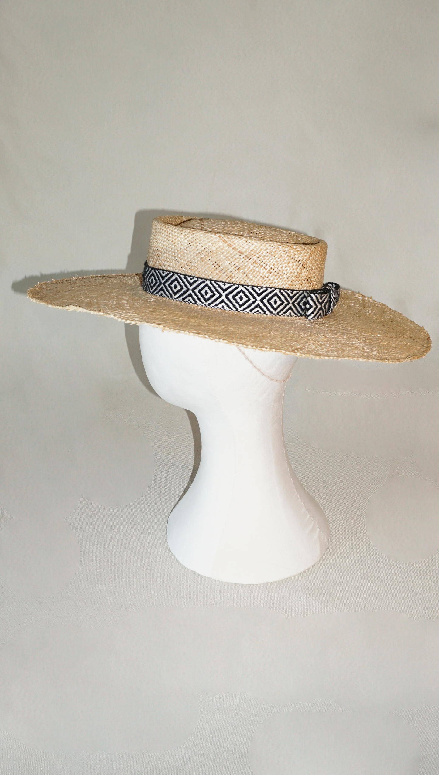 Delos handmade wide brim boater hat, pork pie crown, natural raffia straw,  woven black & ivory geometric band with back bow, left side view by Anna Xaniotaki 