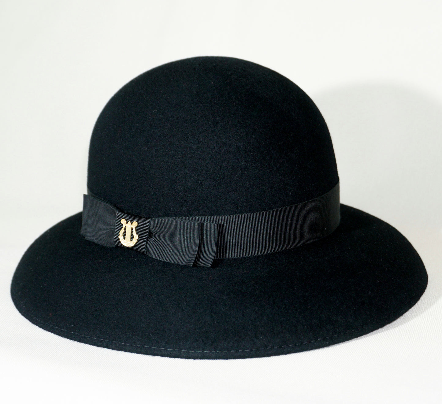 Noir Elegance Hat in Wool Felt with Bow and Gold Lyre by Anna Xaniotaki - three-quarter view