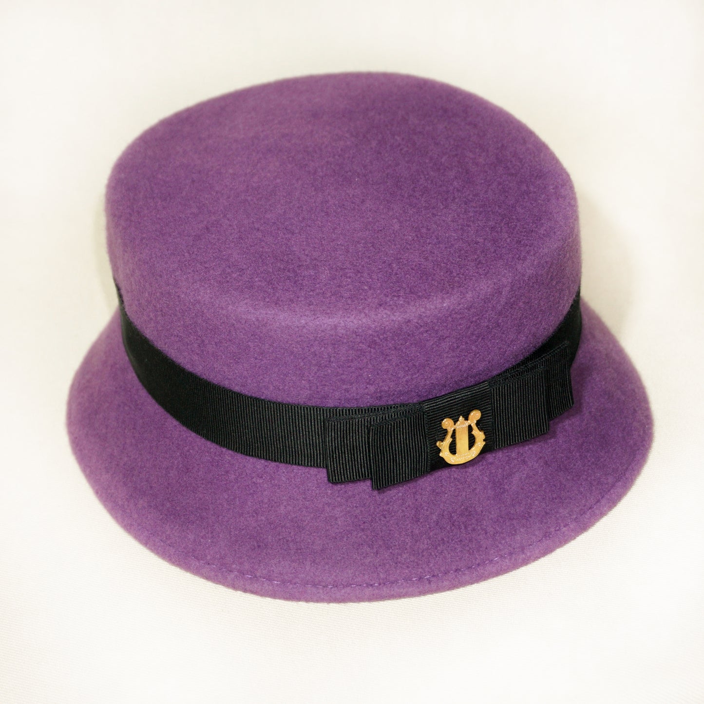Aristocratic Melody Pillbox Hat in Royal Purple Wool Felt with Black Double Bow and Gold Lyre by Anna Xaniotaki - three-quarter view 