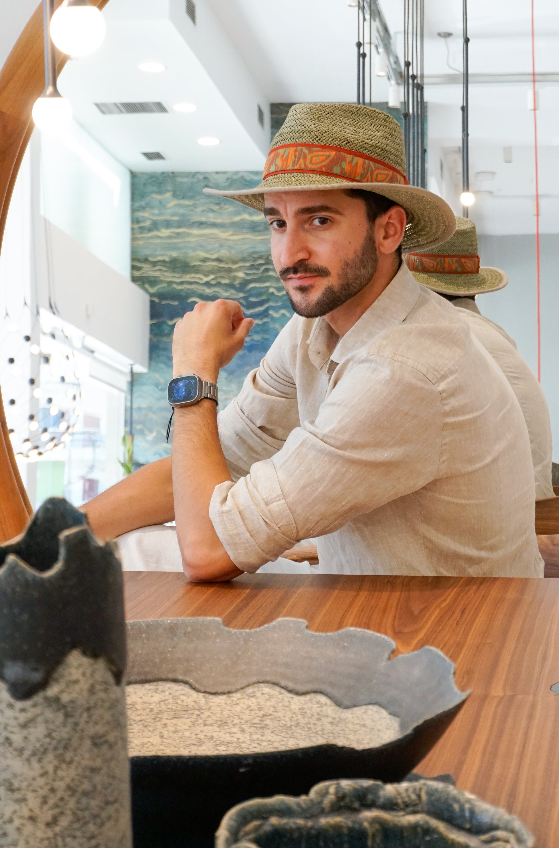 Man wearing the Indy Safari Fedora Hat in olive green paper straw with coral Italian cotton grosgrain ribbon and woven orange, coral and green band, photographed in a three-quarter front left view. Custom made-to-order fedora for summer special occasions, garden parties, vacations or for everyday man's elegance. Bespoke couture millinery by Anna Xaniotaki.