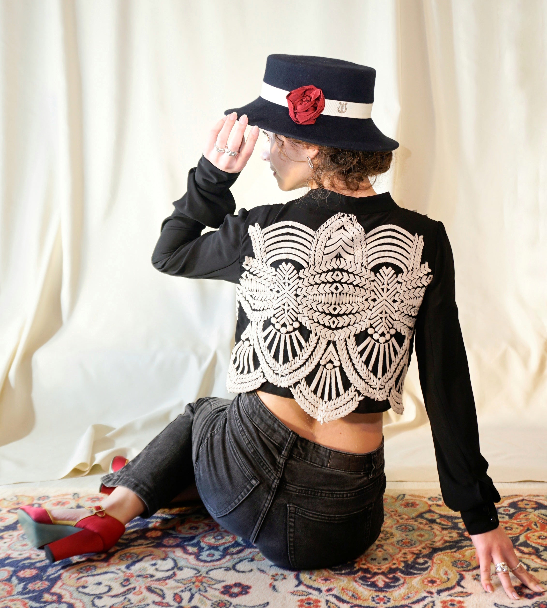 Woman wearing the Rose of the Night Hat in navy fine wool felt with a light cream Italian cotton grosgrain band, a handmade red rose and a 925 sterling silver lyre jewel.