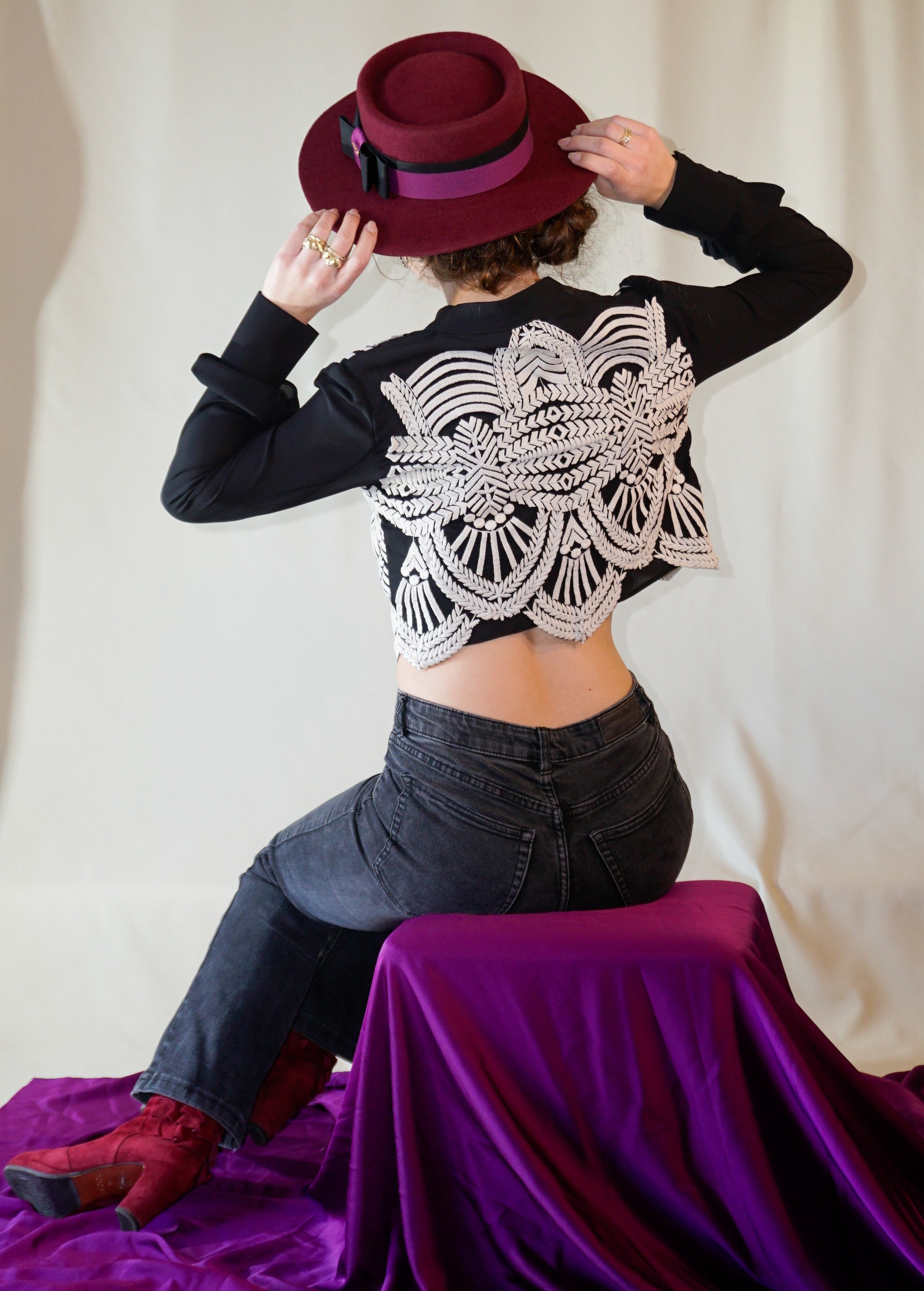 Woman wearing Scarlet Ode burgundy boater hat with black and orchid purple ribbons, double bow and golden lyre by Anna Xaniotaki - back view