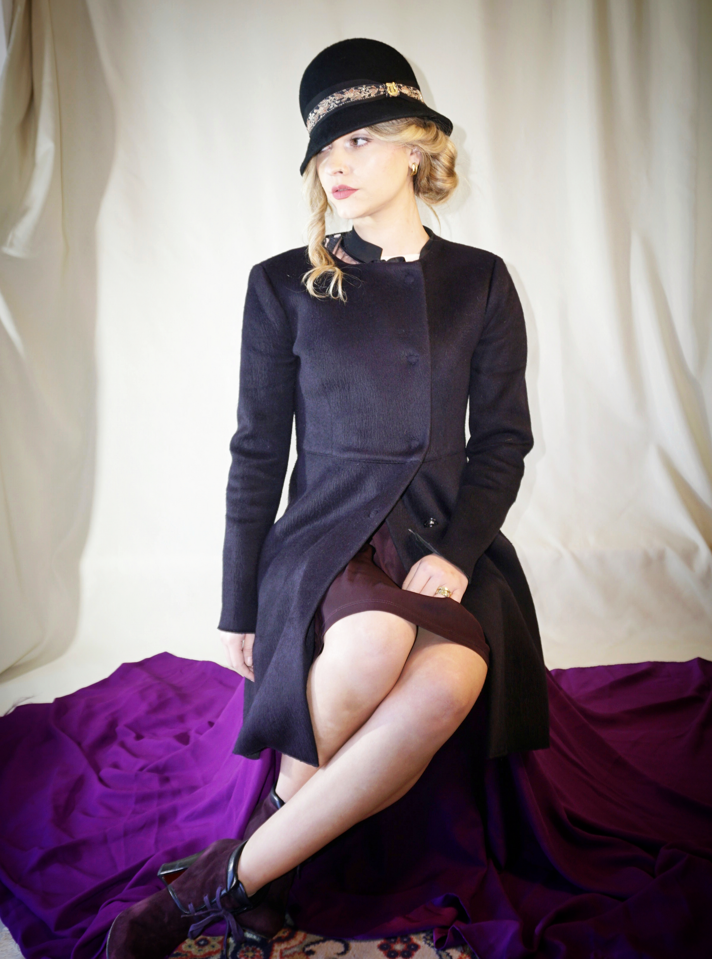 Woman wearing the Vintage Whisper black wool felt cloche hat with a gold lyre emblem, featuring an itallian black grosgrain ribbon and a floral woven ribbon. Three-quarter right side front view. Handcrafted by Anna Xaniotaki