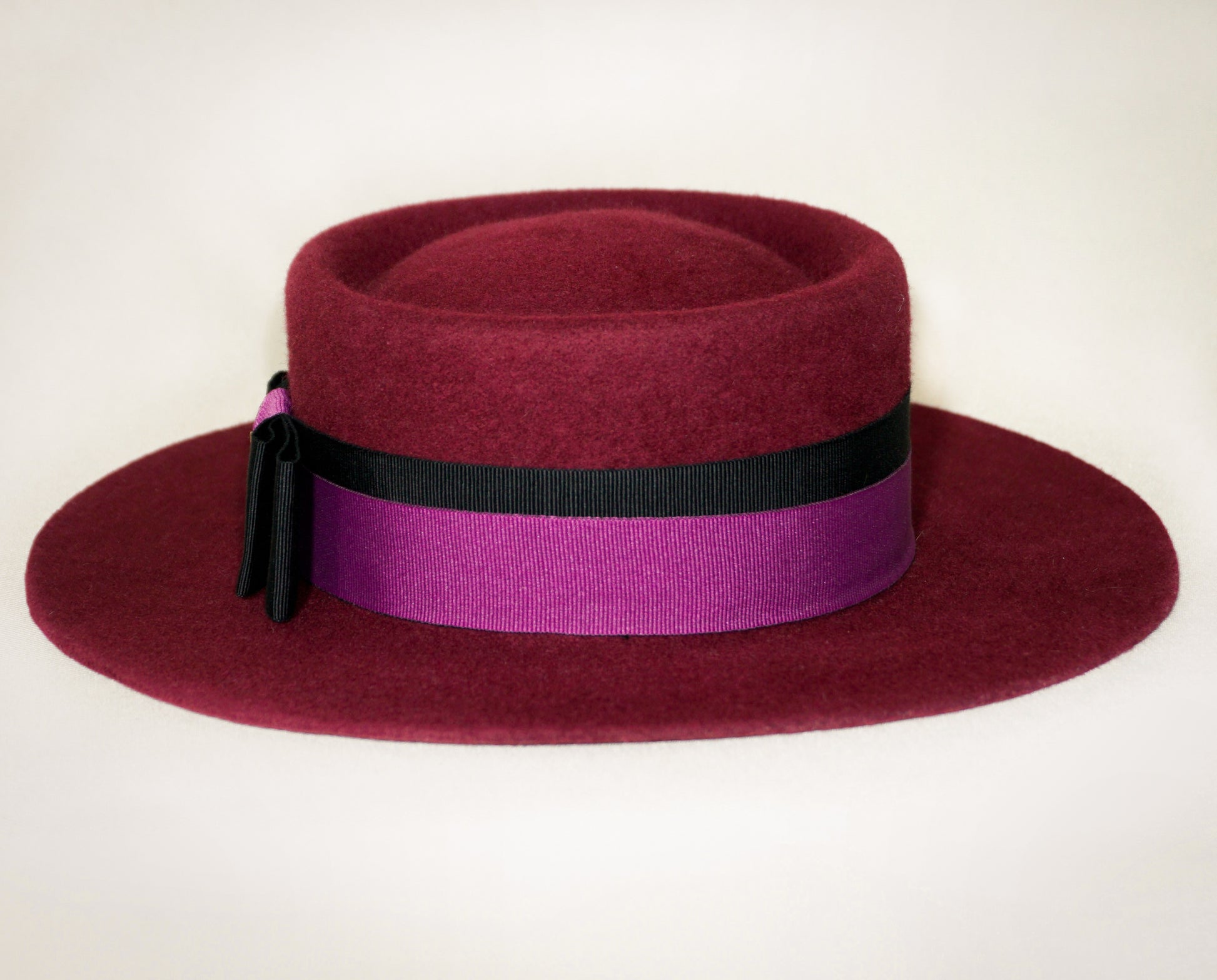 Front view of Scarlet Ode burgundy boater hat with double bow and golden lyre
