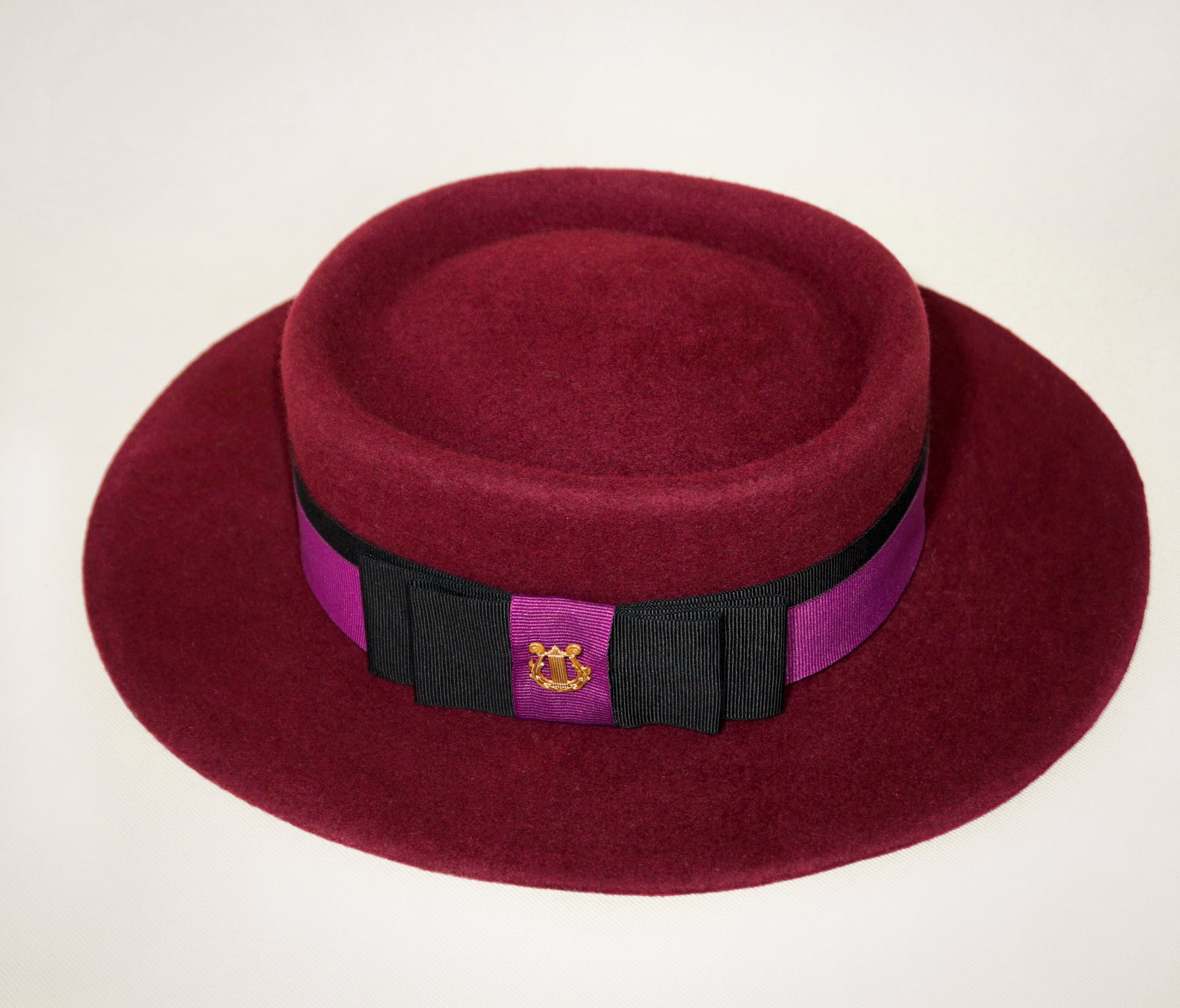 Right side view of Scarlet Ode burgundy boater hat with black and orchid purple ribbons, double bow and golden lyre
