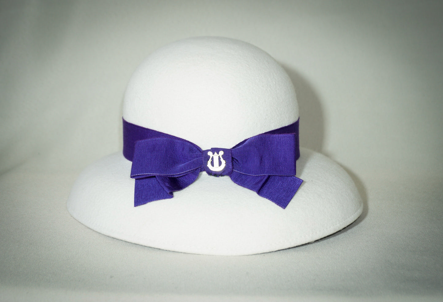 Blanche Élégance white felt hat with purple grosgrain bow and golden lyre by Anna Xaniotaki, right three-quarter front view