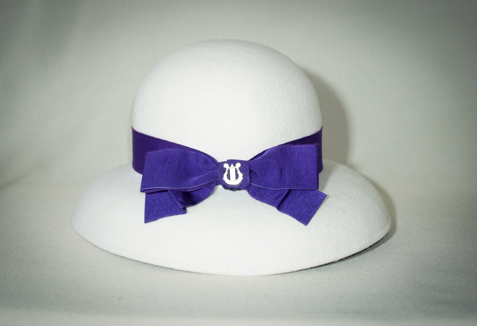 Blanche Élégance white felt hat with purple grosgrain bow and golden lyre by Anna Xaniotaki, right three-quarter front view