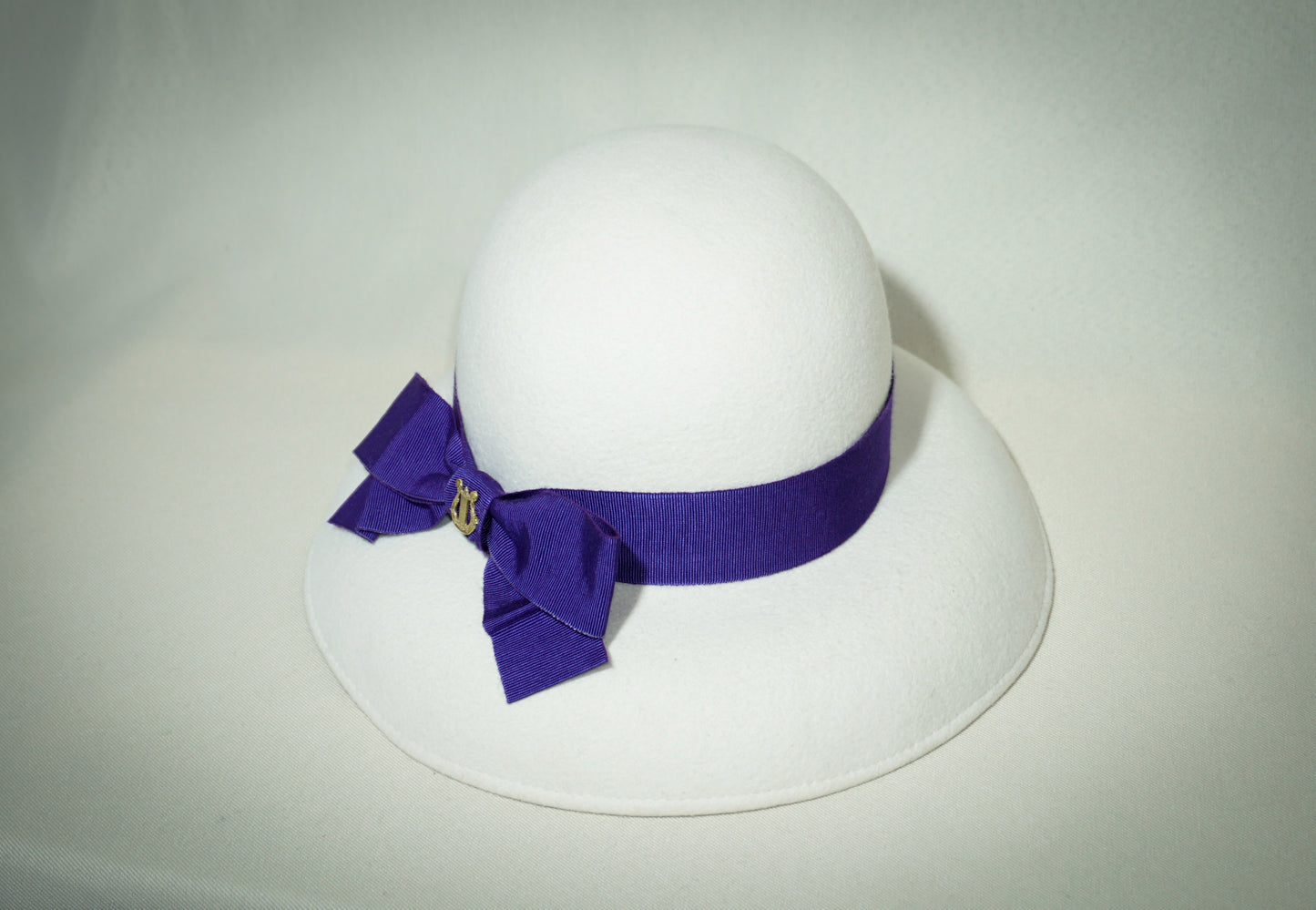Blanche Élégance white felt hat with purple grosgrain bow and golden lyre by Anna Xaniotaki,  front view