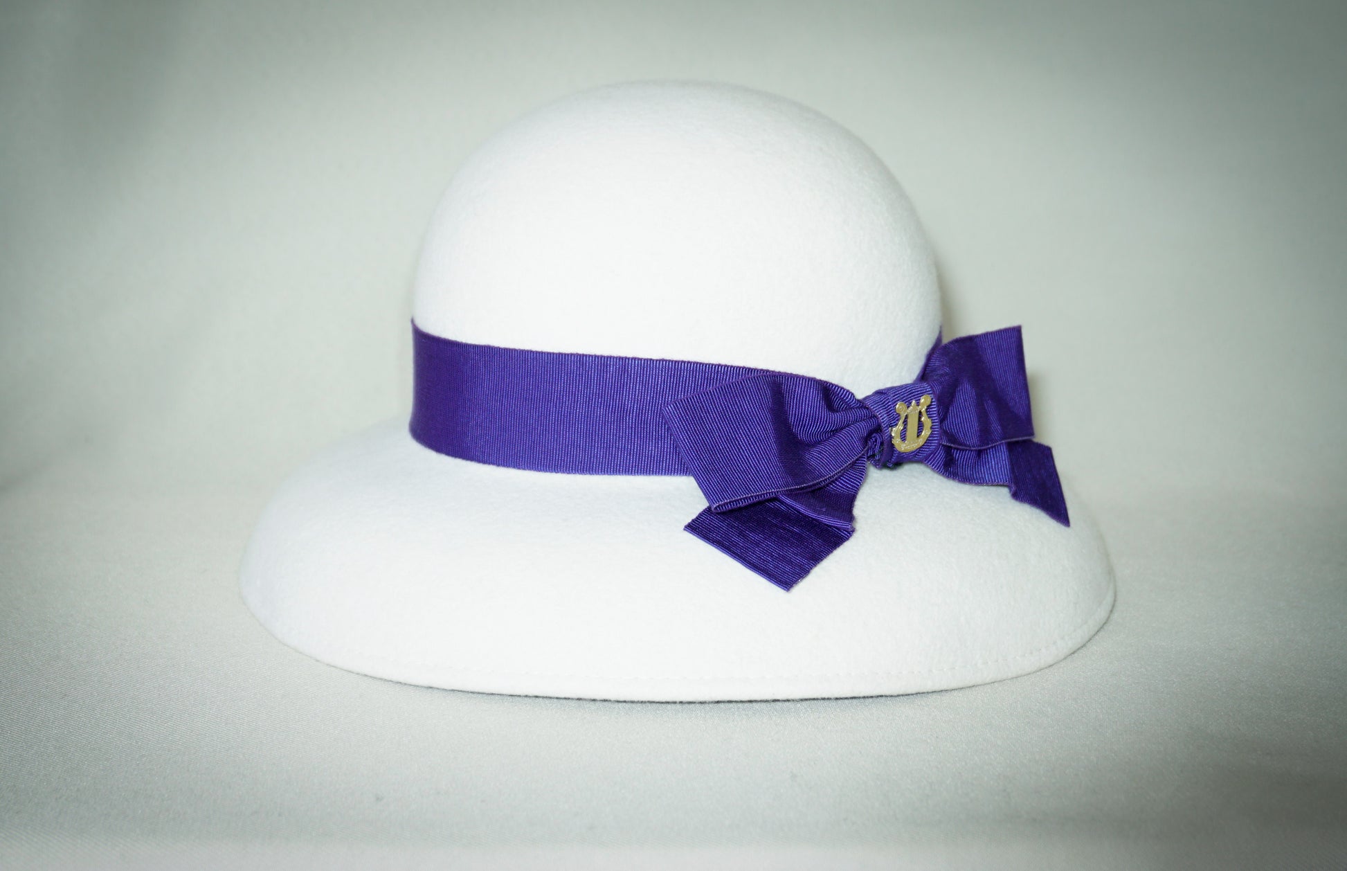 Blanche Élégance white felt hat with purple grosgrain bow and golden lyre by Anna Xaniotaki, right side view