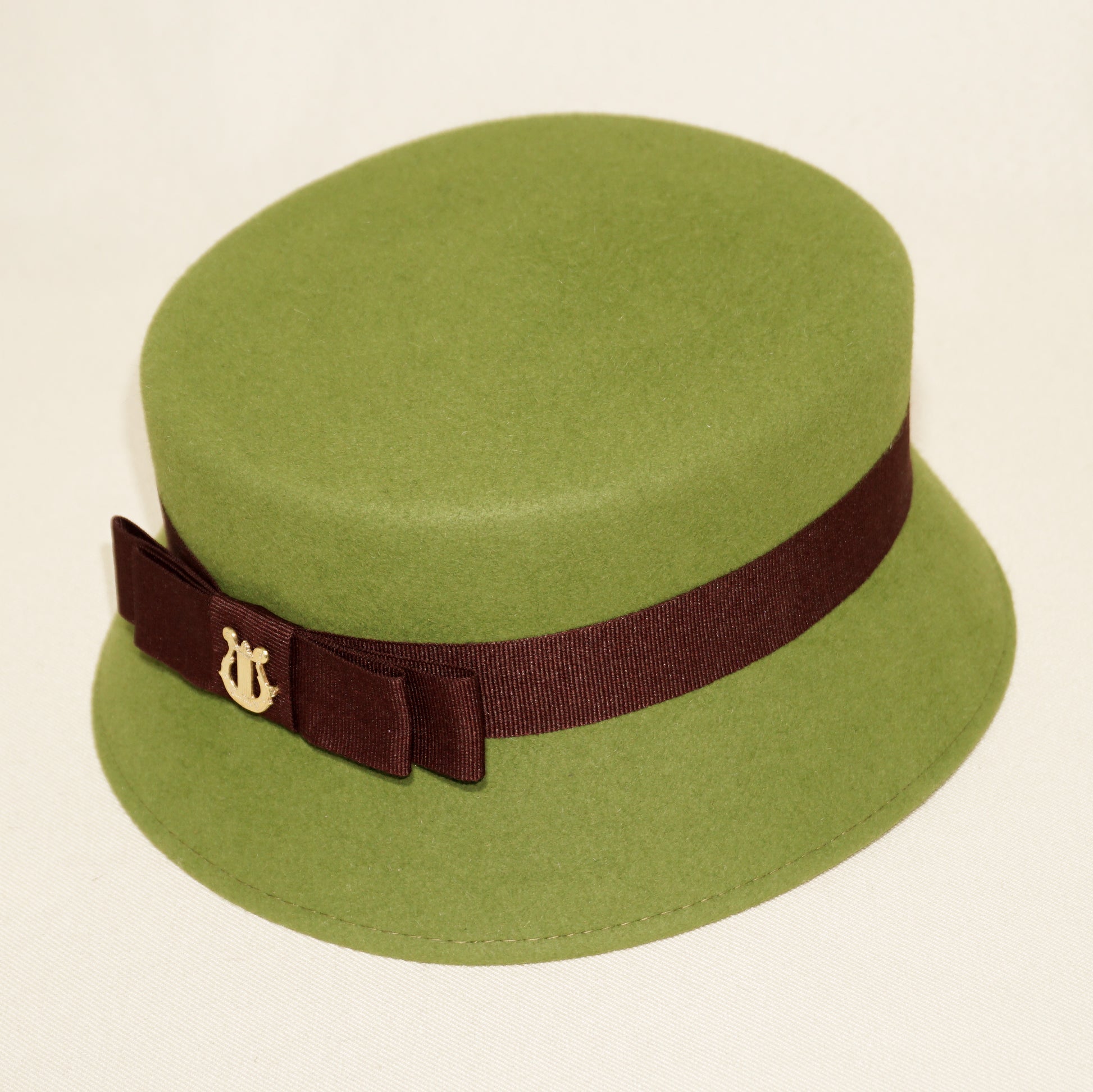 Aristocratic Melody lime pillbox felt hat with double burgundy bow and 14ct gold-plated silver lyre by Anna Xaniotaki - front angle view 
